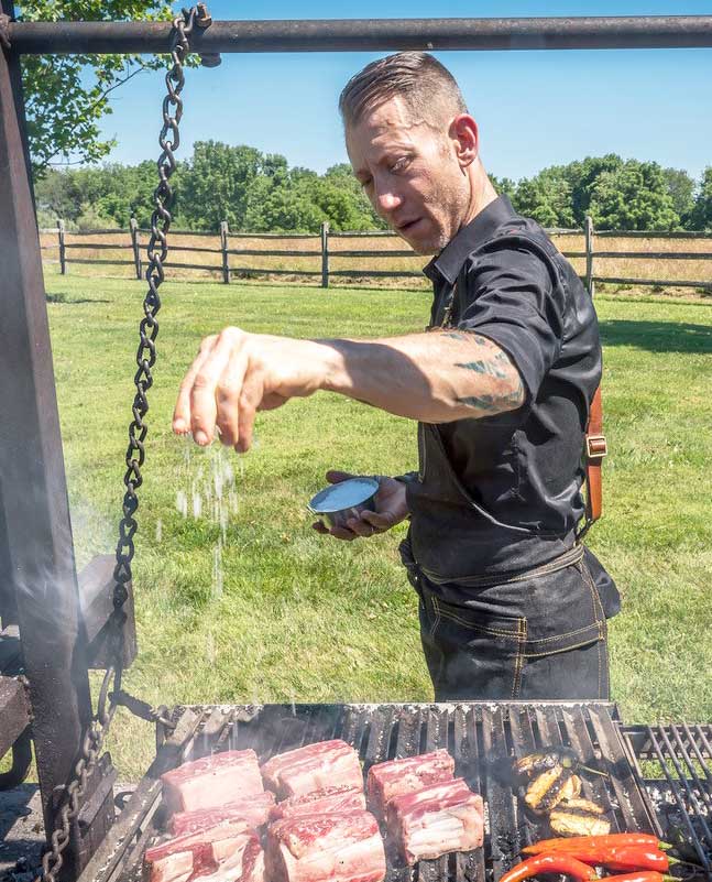 Hugh Mangum at the grill seasoning meat